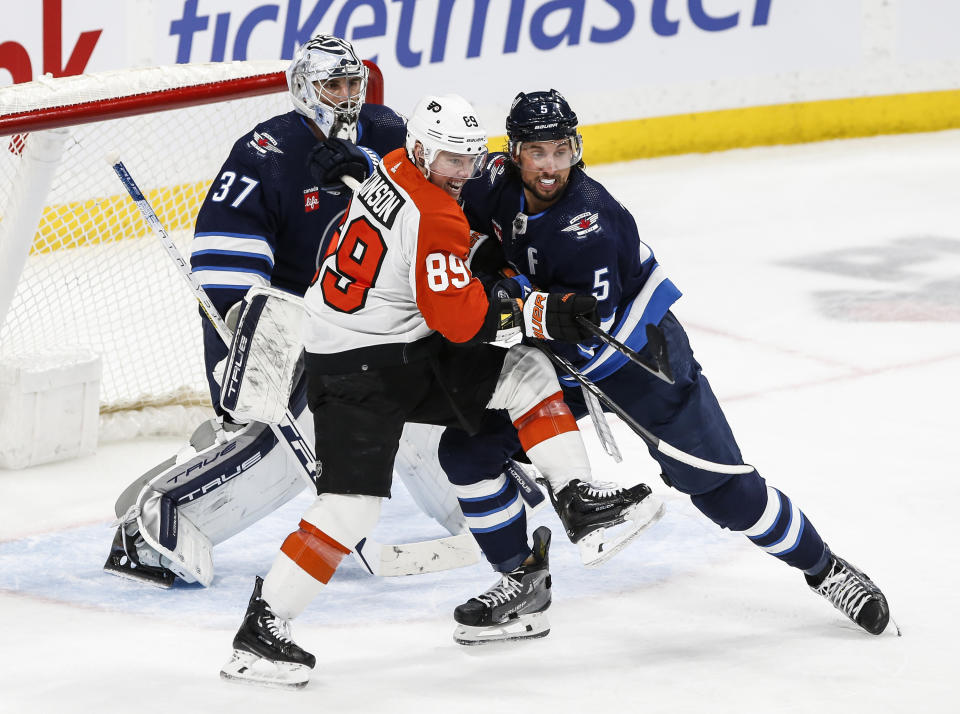 Winnipeg Jets' Brenden Dillon (5) defends against Philadelphia Flyers' Cam Atkinson (89) in front of Jets' goaltender Connor Hellebuyck (37) during second-period NHL hockey game action in Winnipeg, Manitoba, Saturday, Jan. 13, 2024. (John Woods/The Canadian Press via AP)