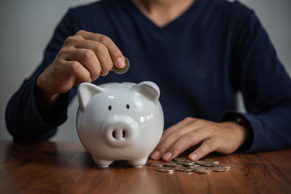 Savings accounts money saving concept man holding coins and throwing them into a piggy bank. Business finance, banking and investment tax accounting