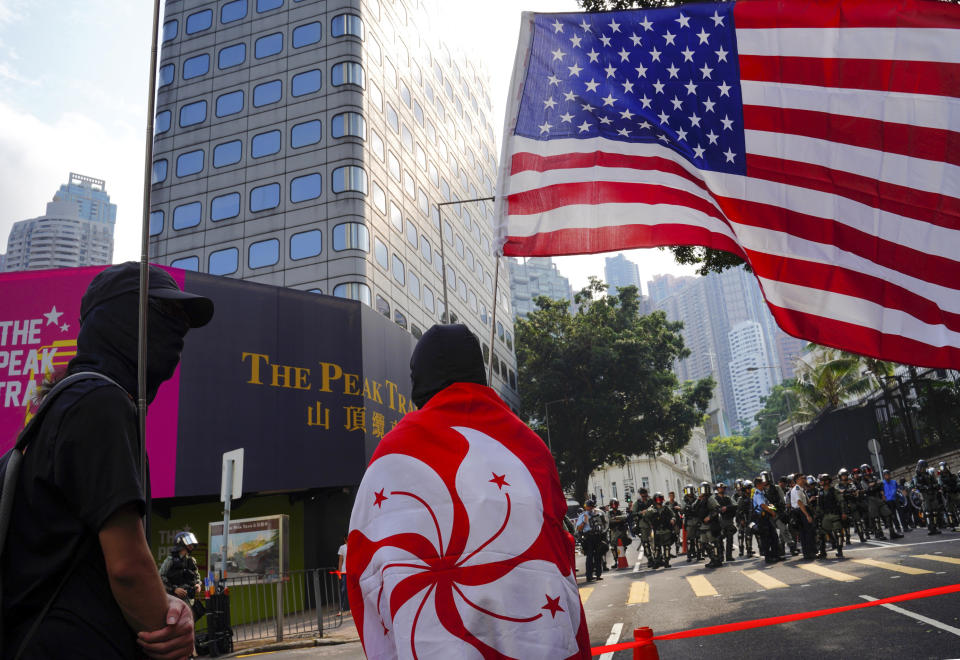 A protester wraps himself with Hong Kong flag, with the U.S. flag seen at right, as they march from Chater Garden to the U.S. Consulate in Hong Kong, Sunday, Sept. 8, 2019. Demonstrators in Hong Kong plan to march to the U.S. Consulate on Sunday to drum up international support for their protest movement, a day after attempts to disrupt transportation to the airport were thwarted by police. (AP Photo/Vincent Yu)