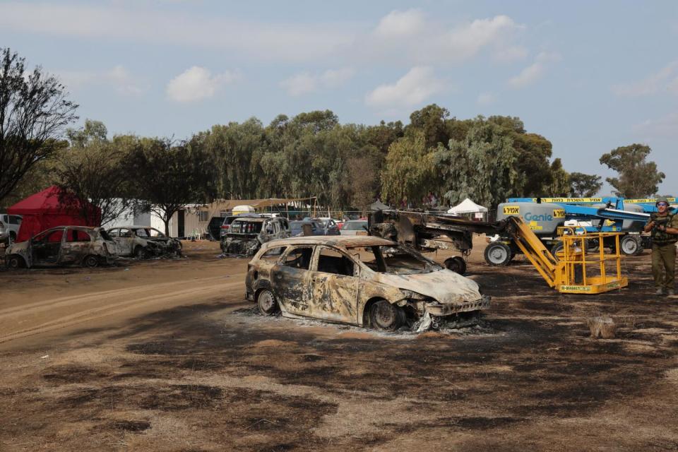 An Israeli soldier walks past burned vehicles in a field.