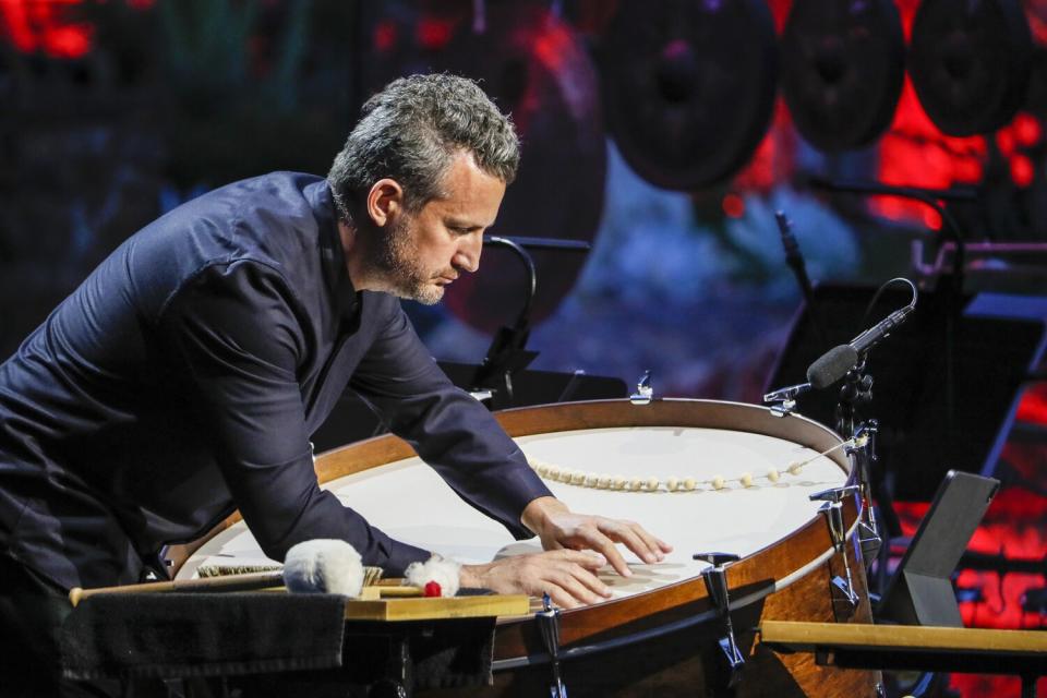 A man taps a large drum with his fingers.