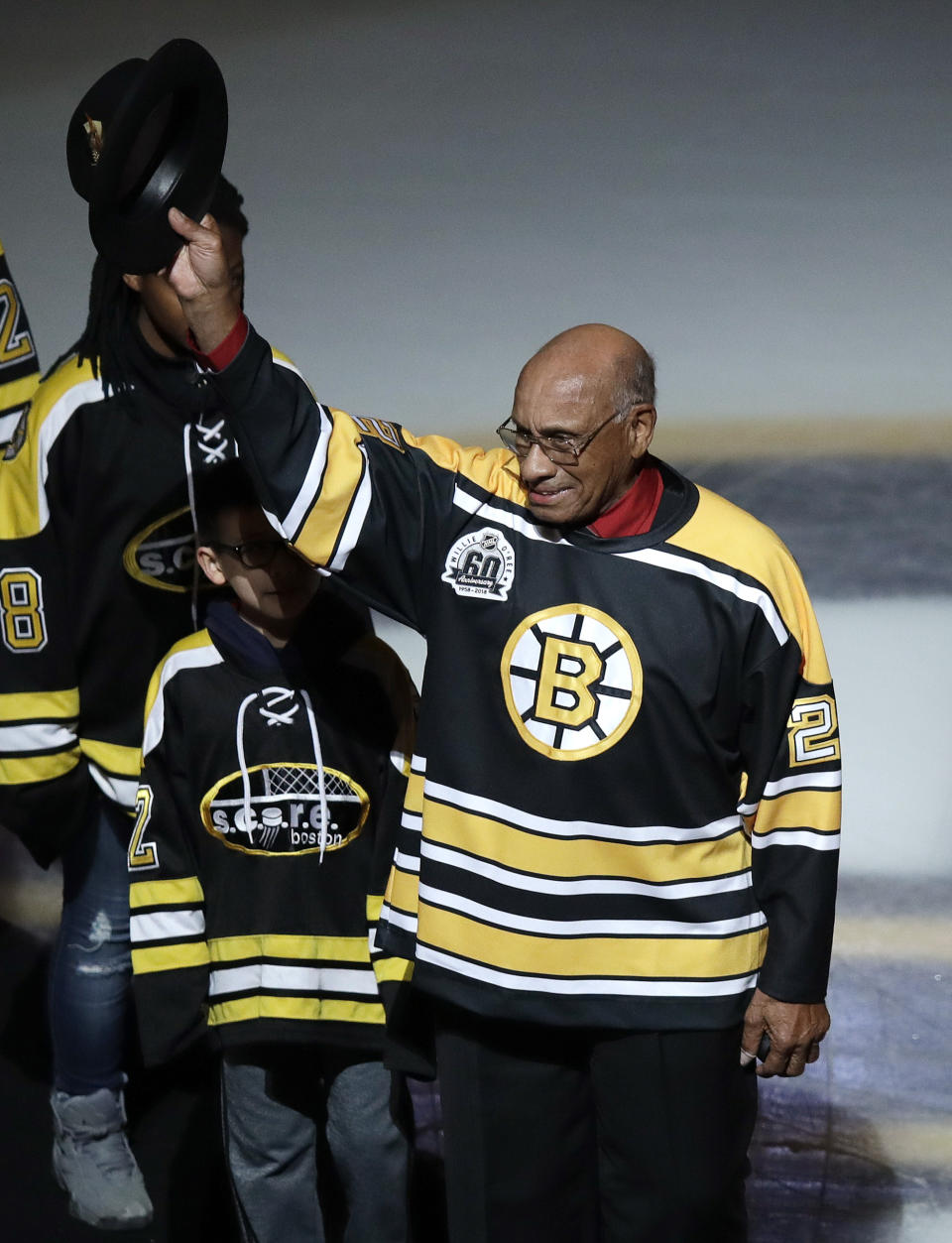 FILE - Former Boston Bruins' Willie O'Ree tips his hat as he is honored prior to the first period of an NHL hockey game against the Montreal Canadiens in Boston, Wednesday, Jan. 17, 2018. O'Ree says the ongoing pandemic hasn't diminished what he says will be a "simply amazing" honor watching his No. 22 jersey retired by the Bruins. O'Ree, who broke the NHL's color barrier on Jan. 18, 1958, was slated to attend when he became the 12th player in team history to have his number retired prior to Boston's game against Carolina on Tuesday, Jan. 18, 2022, But persisting concerns about the pandemic changed those plans. He will now participate from his home in San Diego.(AP Photo/Charles Krupa, File)