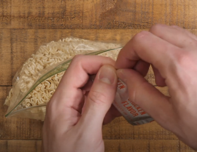 Sprinkling chicken flavor packet on crushed dry ramen in bag