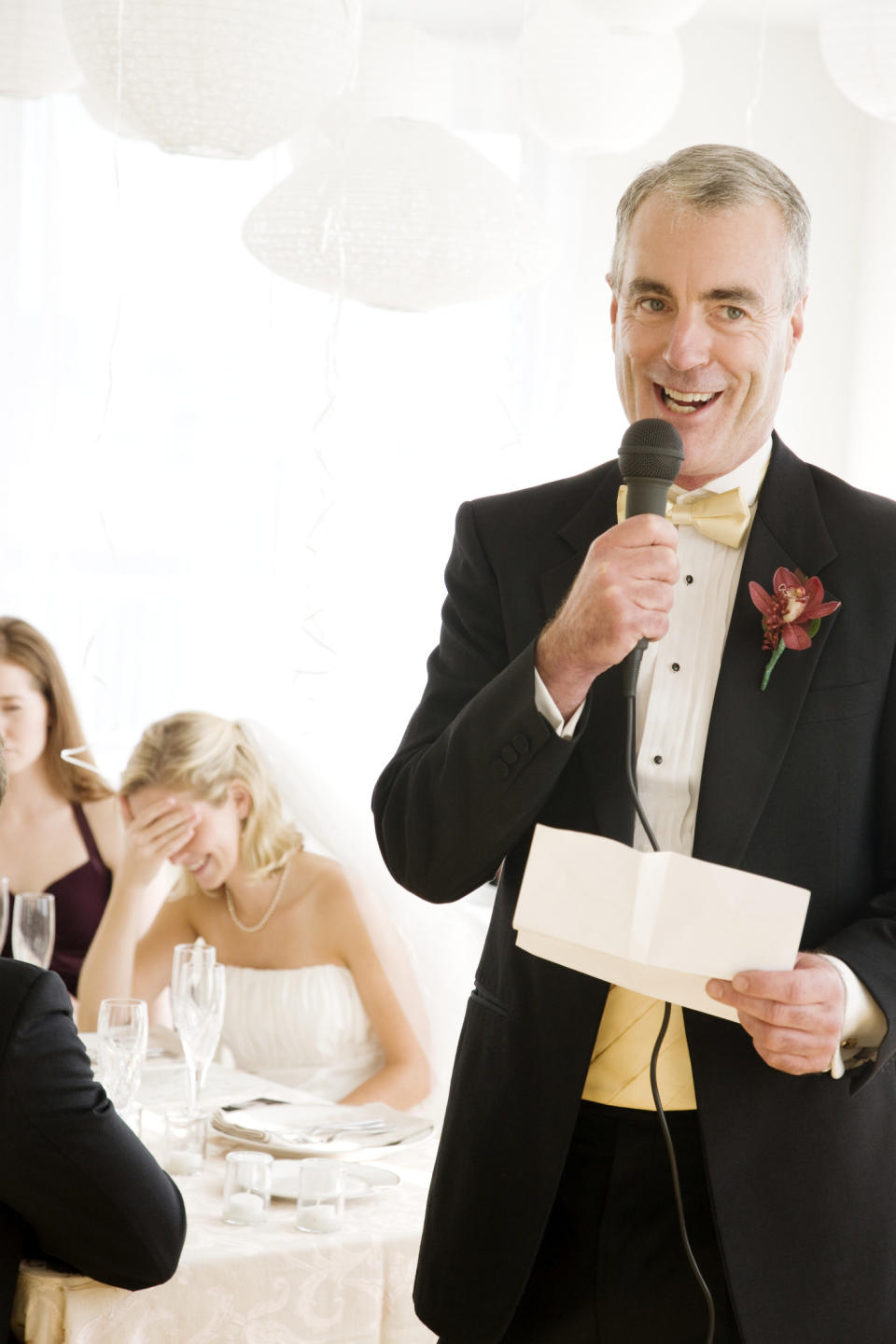 father giving a speech with bride behind him laughs with embarrassment