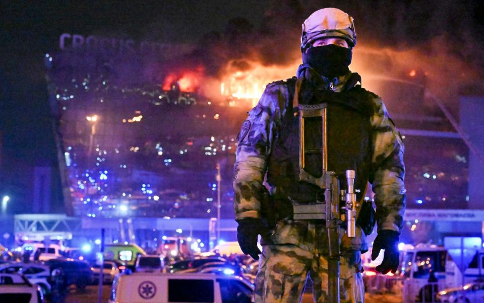 A Russian servicemen patrols the area as the Crocus City Hall burns in the background