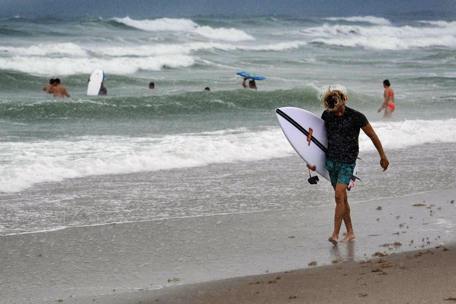 A man carries his surf board through the rain on Cocoa Beach on September 28, 2022, as the eastern coast of central Florida braces for Hurricane Ian. (Photo by Jim WATSON / AFP) (Photo by JIM WATSON/AFP via Getty Images)