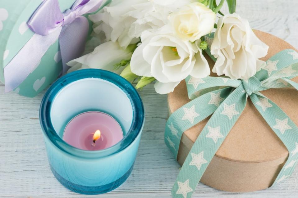 Lit candle in a blue cup next to packaged gifts and flowers