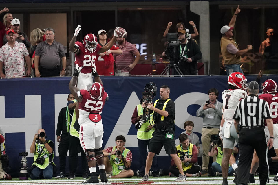 Alabama offensive lineman Tyler Booker (52) lifts Alabama running back Jam Miller (26) after Miller scores a touchdown during the first half of the Southeastern Conference championship NCAA college football game against Georgia in Atlanta, Saturday, Dec. 2, 2023. (AP Photo/Mike Stewart)