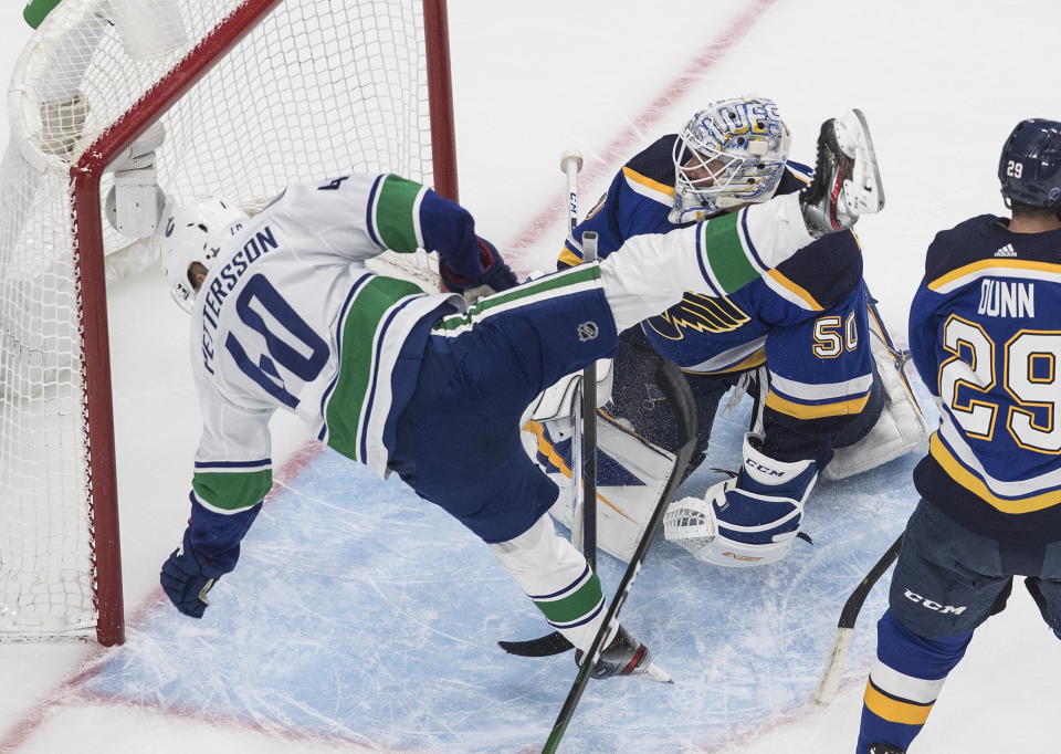 Vancouver Canucks' Elias Pettersson (40) falls over St. Louis Blues goalie Jordan Binnington (50) during the first period of an NHL hockey Stanley Cup first-round playoff series, Friday, Aug. 14, 2020, in Edmonton, Alberta. (Jason Franson/The Canadian Press via AP)