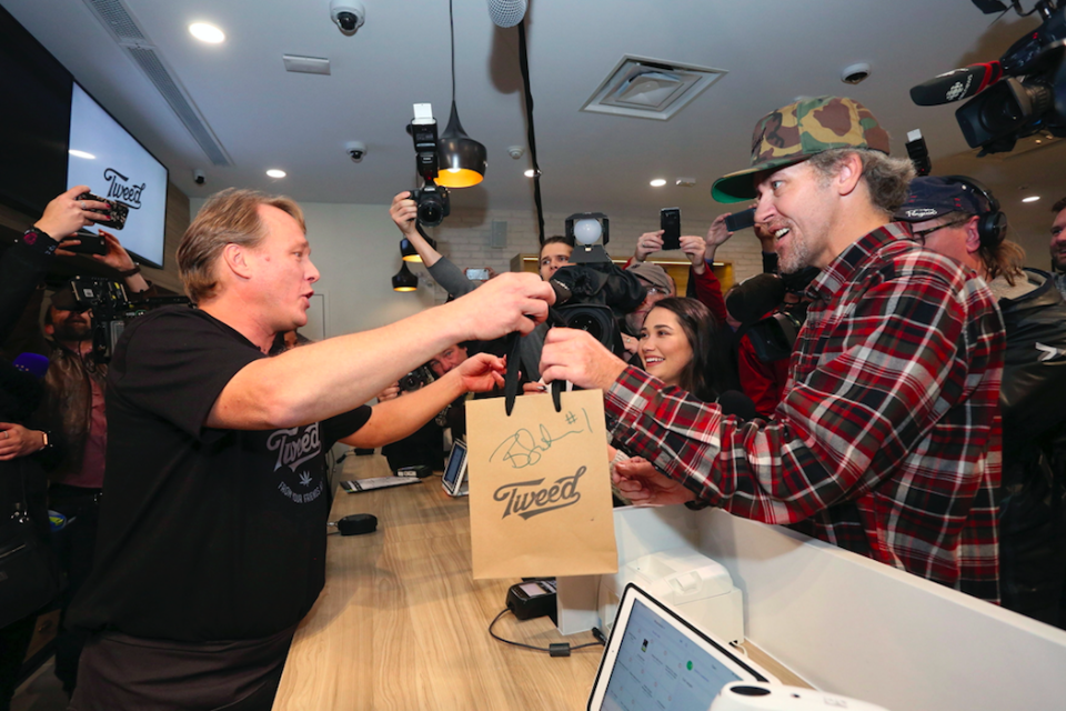 <em>Canopy Growth CEO Bruce Linton (left) passes a bag with the first legal cannabis for recreation use sold in Canada to Nikki Rose and Ian Power at the Tweed shop (AP)</em>