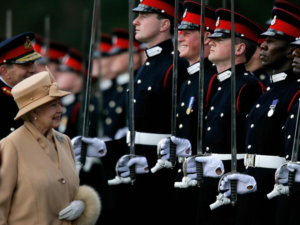 Queen Elizabeth walks by a line of soldiers, including Prince Harry, who is cracking a smile at the sight of his grandmother.