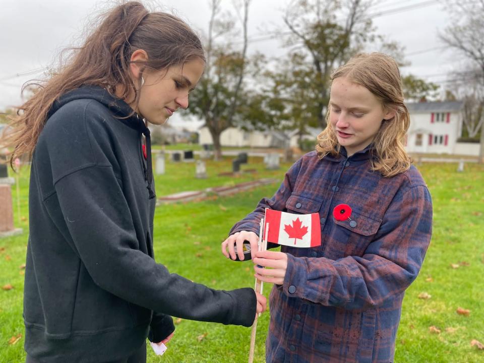 Austyn MacPhee, right, and Montana Arsenault put up new Canadian flags at St. Paul's Cemetery in Summerside.