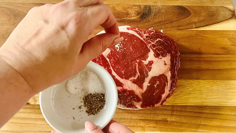 hand sprinkling salt and pepper on steak