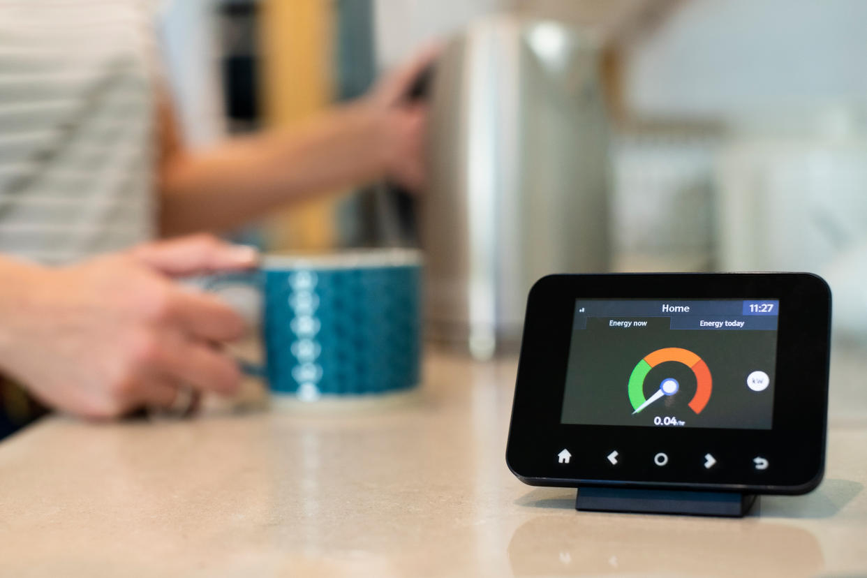 Woman At Home Boiling Kettle For Hot Drink With Smart Energy Meter In Foreground