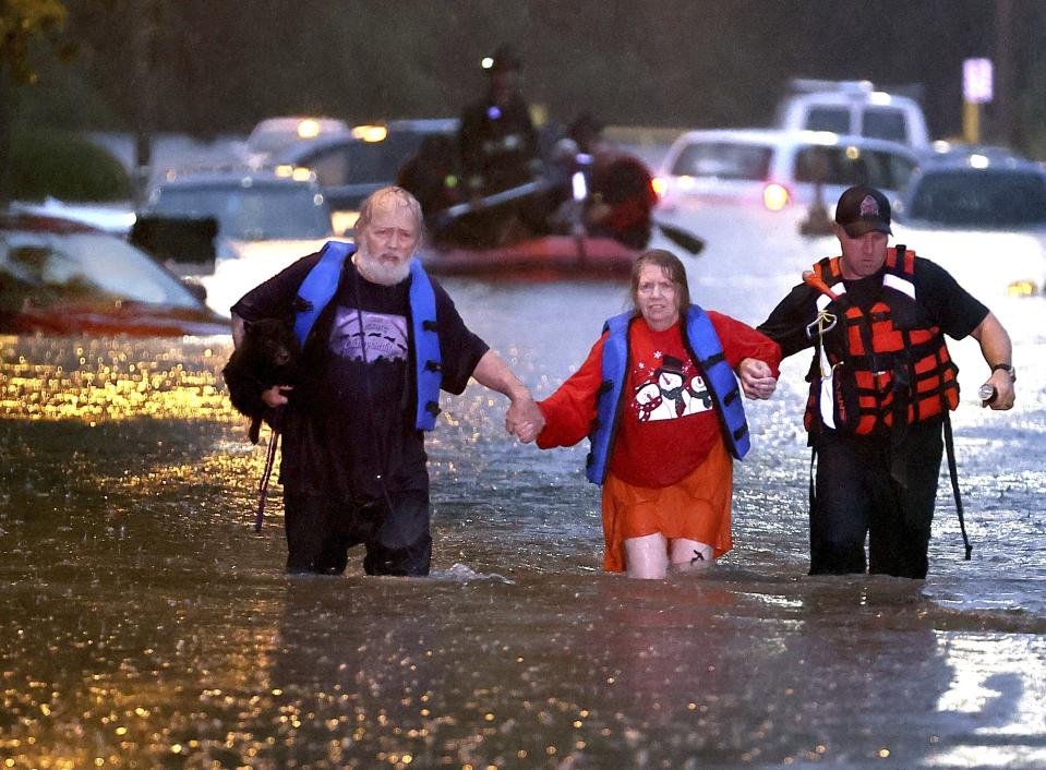 John Ward, left, and a firefighter help Lynn Hartke wade through the flash floodwater on Hermitage Avenue in St. Louis on Tuesday, July 26, 2022. (David Carson/St. Louis Post-Dispatch via AP)
