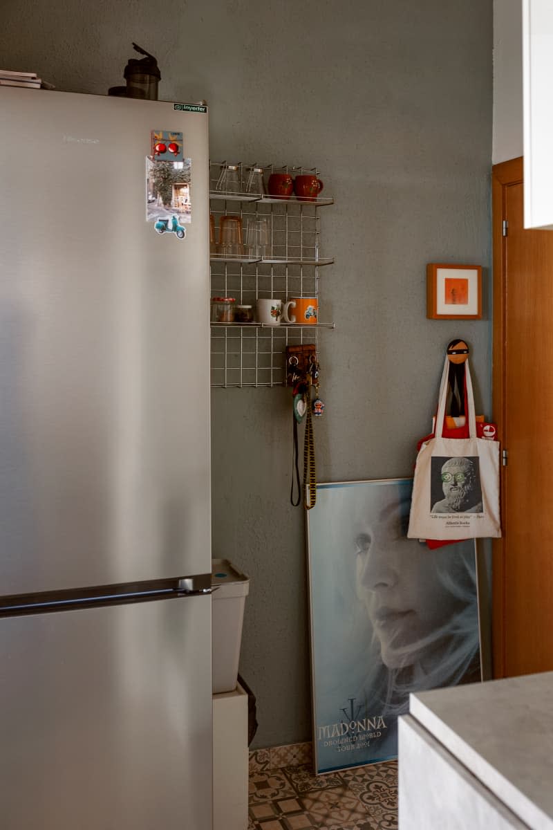 Refrigerator and drinkware shelf on gray kitchen wall.