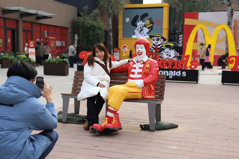 A woman sitting next to a statue of ''Ronald McDonald", the McDonald's company mascot, poses for pictures outside the McDonald's themed exhibition in Beijing