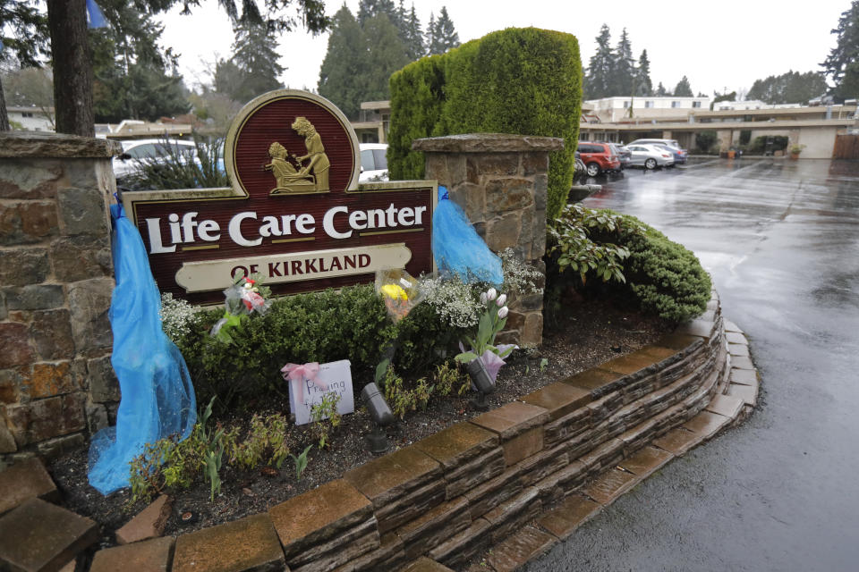 Flowers and other memorials are viewed Friday, March 13, 2020, near a sign at the entrance to the Life Care Center in Kirkland, Wash., near Seattle, which has been at the center of the coronavirus outbreak in the state. Residents of assisted living facilities and their loved ones are facing a grim situation as the coronavirus spreads across the country, placing elderly people especially at risk. (AP Photo/Ted S. Warren)