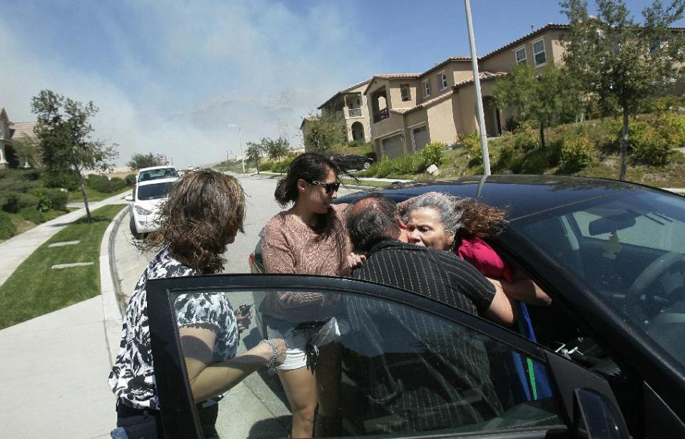 Javier Romero helps his mother-in-law Sarah Robles into a car while Sandy Romero, left, and Brittany Romero help as they evacuate their home to get out of the way of a brush fire burning in Day Creek near the Etiwanda Preserve in Rancho Cucamonga, Calif., Wednesday, April 30, 2014. Fire officials say winds gusting to 60 mph are pushing the flames through the foothills of the San Bernardino Mountains east of Los Angeles, although no homes are in immediate danger. Several neighborhoods and at least seven schools in Rancho Cucamonga have been evacuated. There’s no word on what sparked the blaze but it comes in the midst of a heat wave that’s created extreme fire danger. (AP Photo/The Press-Enterprise, Stan Lim) MAGS OUT; MANDATORY CREDIT