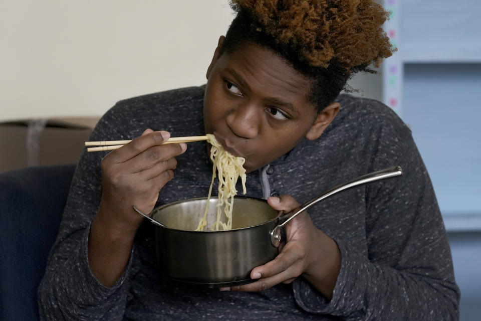 Nehemiah Powell, 14, watches TV and eats noodles Saturday, Nov. 21, 2020, following his virtual school gym workout at his home in Skokie, Ill. After his mother's employer eliminated her job, the family is moving to Georgia where living costs are lower. (AP Photo/Charles Rex Arbogast)