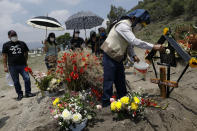 David Gonzalez uses a flower to sprinkle holy water onto the grave of his wife, Luz Maria Gonzalez, as they mark the 9th day since her burial in the Municipal Cemetery of Valle de Chalco on the outskirts of Mexico City, Saturday, July 4, 2020. Gonzalez, 56, who had long suffered from asthma, diabetes, and hypertension, died two days after her 29-year-old son, who was hospitalized for breathing problems and a cough before dying of complications said to be related to pneumonia and undiagnosed diabetes. (AP Photo/Rebecca Blackwell)
