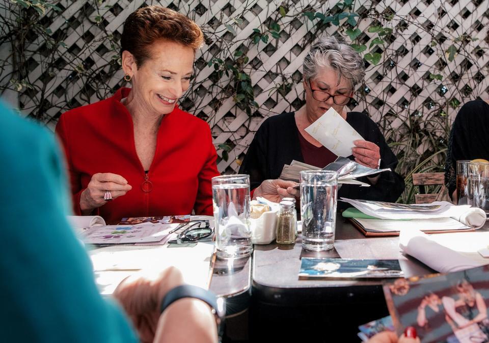 People look at photos and papers spread on a patio dining table.