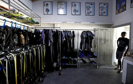 Nuwan Harshana, 31, manager at Pearl Divers, a diving school, looks on next to the diving costumes and equipment room at the hotel at Unawatuna beach in Galle