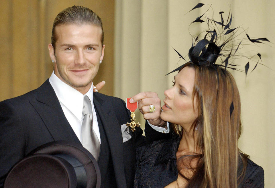 David Beckham stands with his wife, Victoria, as he shows off the OBE (Officer of the Order of the British Empire)  he received 27 November , 2003, from Britain's Queen Elizabeth II at London's Buckingham Palace. The former Manchester United star, who now plays for Real Madrid, said recently: 'I am honoured and privileged to receive this recognition. It's not just for me but for Manchester United, England, all of my teammates and my family'. (Fiona Hanson / POOL / AFP via Getty Images)