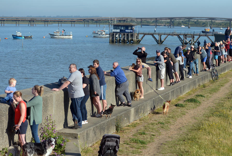 People line the sea wall to watch as the boat heads into the port to deliver goods.