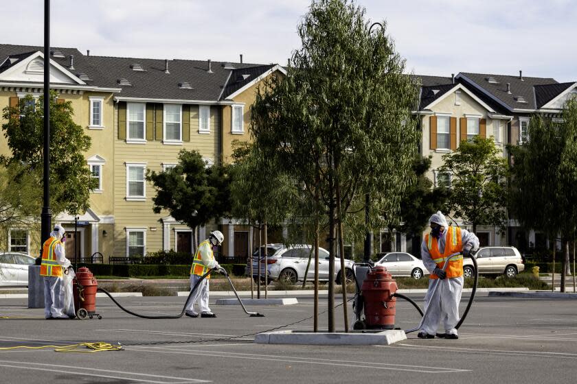 Tustin, CA - November 13: A disaster cleanup crew vacuums up potentially-toxic debris from the historic Tustin hangar at Veterans Sports Park next to a condo neighborhood across the street from the still-burning WWII-era blimp hangar at the former air base in Tustin Monday, Nov. 13, 2023. Flare-ups and toxic air from last week's destructive hangar fire in Tustin continue to cause trouble for nearby residents. The City of Tustin took to X, formerly Twitter, to confirm that the western wall of the 17-story building reignited Sunday night. Orange County Fire Authority personnel remained on the scene keeping watch of the blaze on Monday morning, with one firefighter telling KTLA 5's Annie Rose Ramos that all they could do was let it burn out. (Allen J. Schaben / Los Angeles Times)