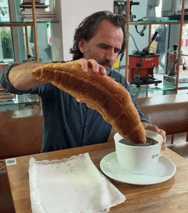 A man dips a giant croissant into a big cup of coffee