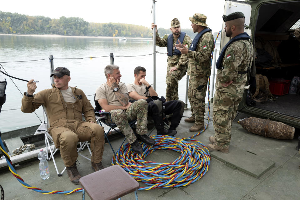 Belgian and Hungarian soldiers rest on a diving platform floating on the Danube River in Budapest, Hungary, Friday, Oct. 13, 2023, during an international training exercise which prepares military divers to find and remove unexploded underwater ordnances. Hungary this year hosted the 10-day exercise for the second year in a row and provided the soldiers from Hungary, Germany, Belgium and Lithuania with hands-on training in a variety of environments, like facing the powerful current of the Danube River. (AP Photo/Bela Szandelszky)