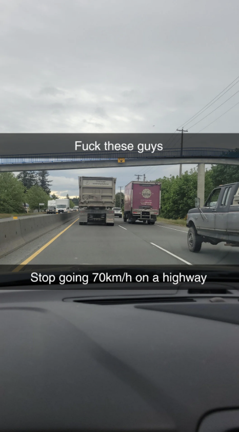 View from a car on the highway showing a white truck and a pink truck. Text overlay reads: "Fuck these guys. Stop going 70km/h on a highway."