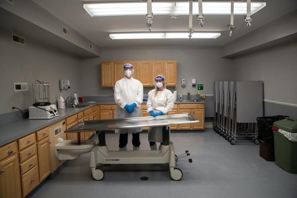 A funeral home director and an intern stand by a mortuary table. <a href="https://www.gettyimages.com/detail/news-photo/funeral-director-alexandra-burke-and-intern-vincent-news-photo/1248738963" rel="nofollow noopener" target="_blank" data-ylk="slk:John Moore/Getty Images News via Getty Images;elm:context_link;itc:0;sec:content-canvas" class="link ">John Moore/Getty Images News via Getty Images</a>