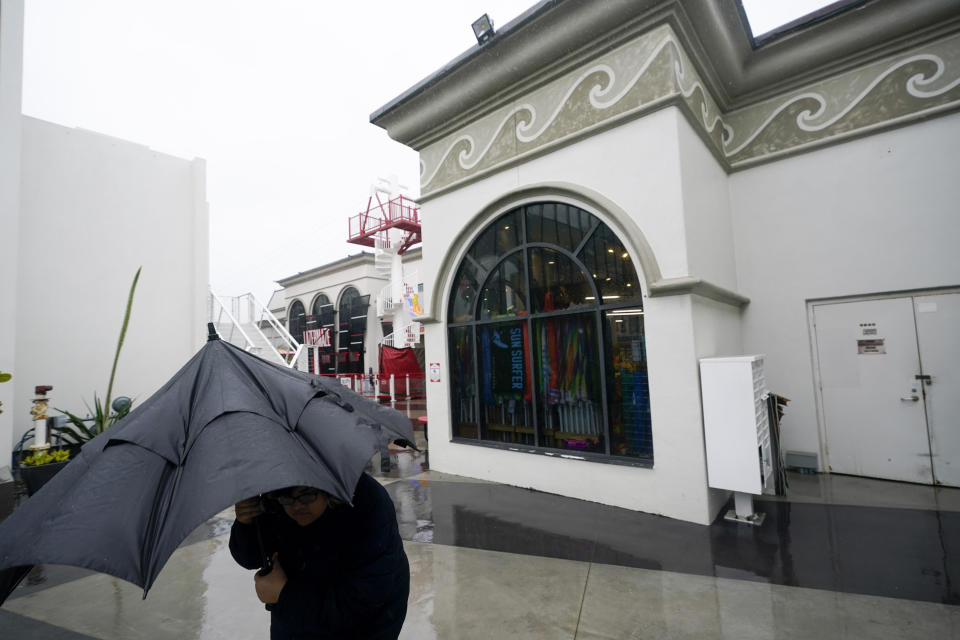 A woman walks under an umbrella at a vacant Belmont Park as rain engulfs the area, Tuesday, March 21, 2023, in San Diego. Californians are tired. Tired of the rain, tired of the snow, tired of stormy weather and the cold, relentlessly gray skies that have clouded the Golden State nearly nonstop since late December. (AP Photo/Gregory Bull)