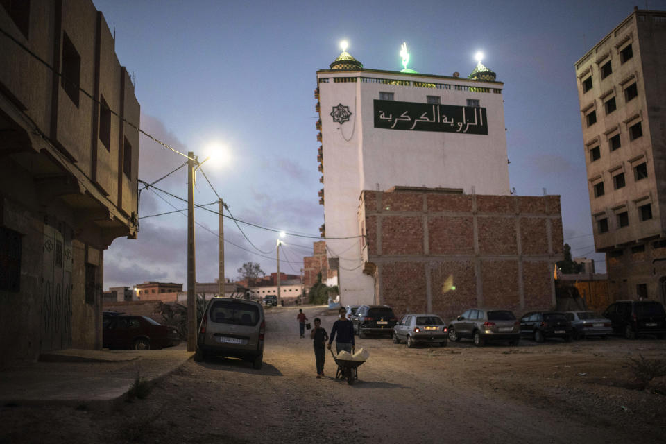 People walk past the headquarters of the Sufi Karkariya order as it is lit during a religious celebration of the prophet Muhammed's birthday, in Aroui, near Nador, eastern Morocco, Monday, Oct. 18, 2021. (AP Photo/Mosa'ab Elshamy)