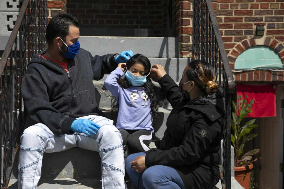 Roberto, left, and Janeth, right, adjust a face mask for their daughter Allison, 5, Tuesday, April 21, 2020, outside their rented basement apartment in Washington. The family has placed a red towel in their doorway hoping that the "angel of death will pass over our home," says Janeth. Since this image was taken Janeth and her husband Roberto, as well as her sister Arely, have been diagnosed with COVID-19. (AP Photo/Jacquelyn Martin)