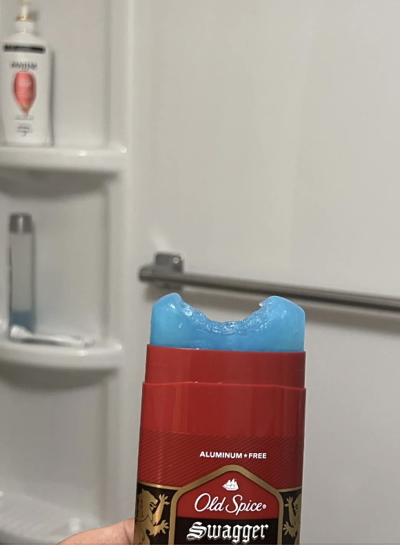 A stick of Old Spice Swagger deodorant with a bite mark. Shower products are visible on a bath shelf in the background