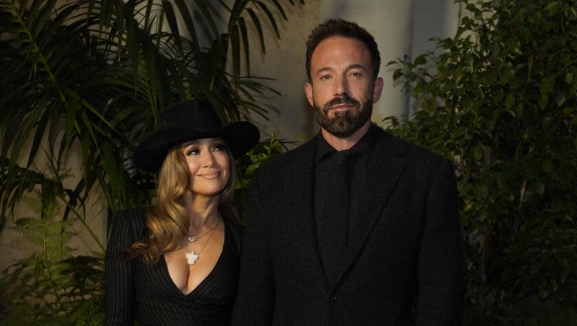 Jennifer Lopez in a black hat, plunging black dress looking at Ben Affleck in a black suit