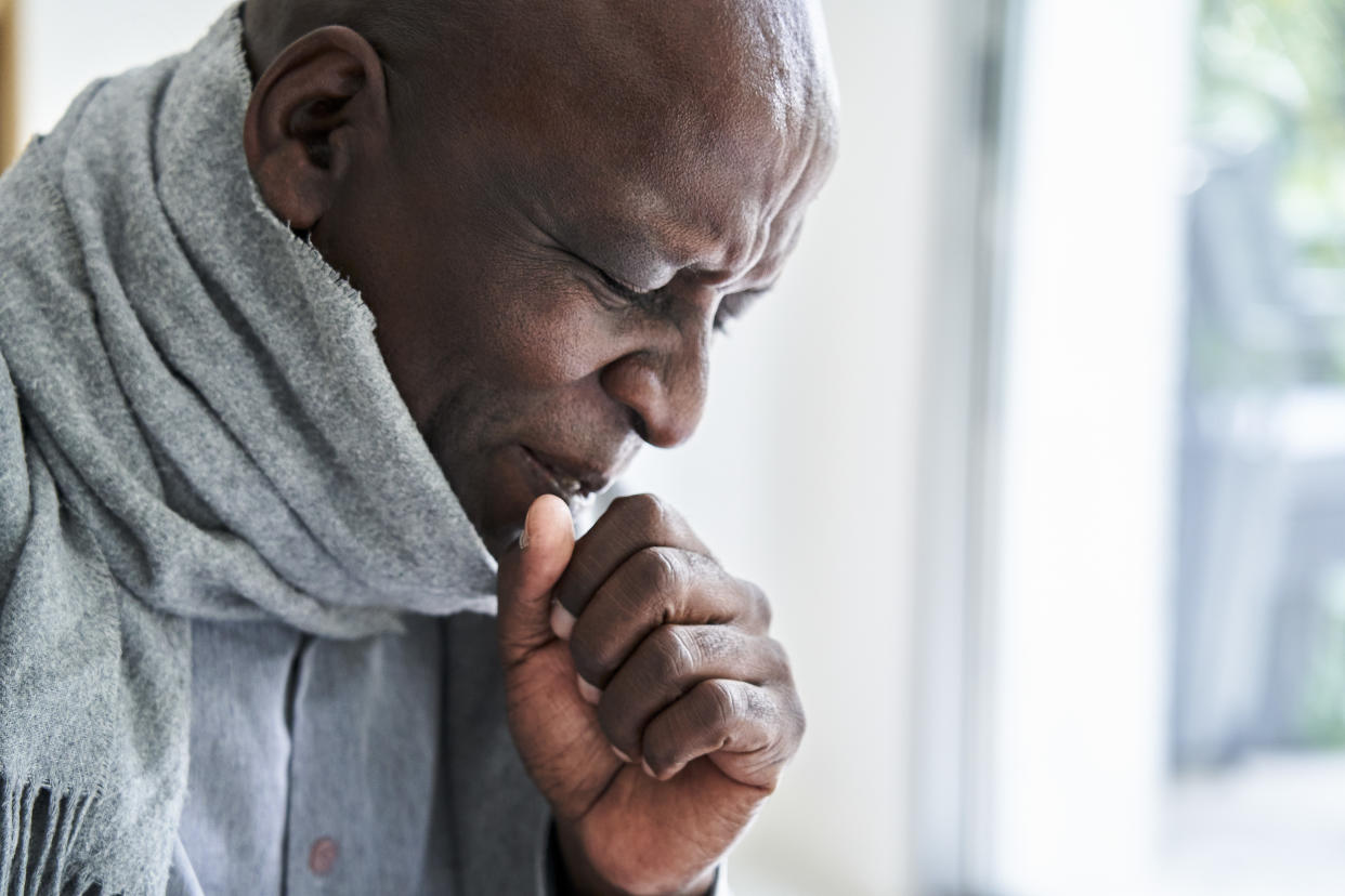 African-American man coughing in his hand and wearing a scarf
