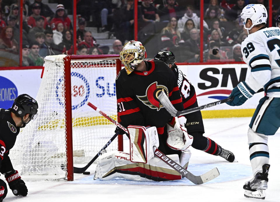 Ottawa Senators goaltender Anton Forsberg (31) looks back as Senators defenseman Jake Sanderson (85) uses his stick to make a save as the puck slides along the goal line and San Jose Sharks center Logan Couture (39) watches during third-period NHL hockey game action in Ottawa, Ontario, Saturday, Dec. 3, 2022. (Justin Tang/The Canadian Press via AP)