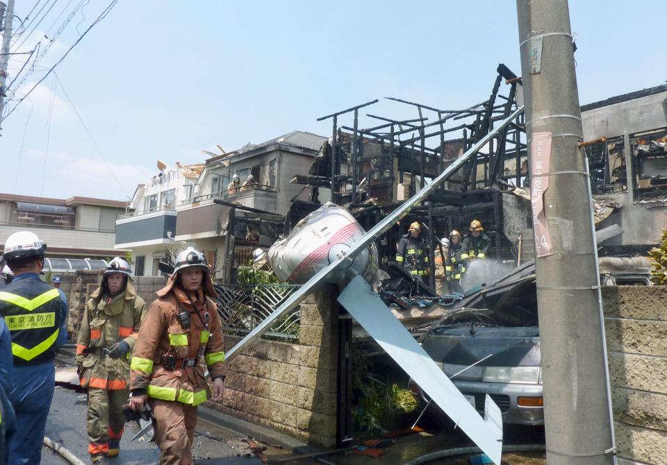 The tail section of a crashed light plane and burning house are seen after the plane went down in a residential area and burst into flames, in Chofu, outskirt of Tokyo