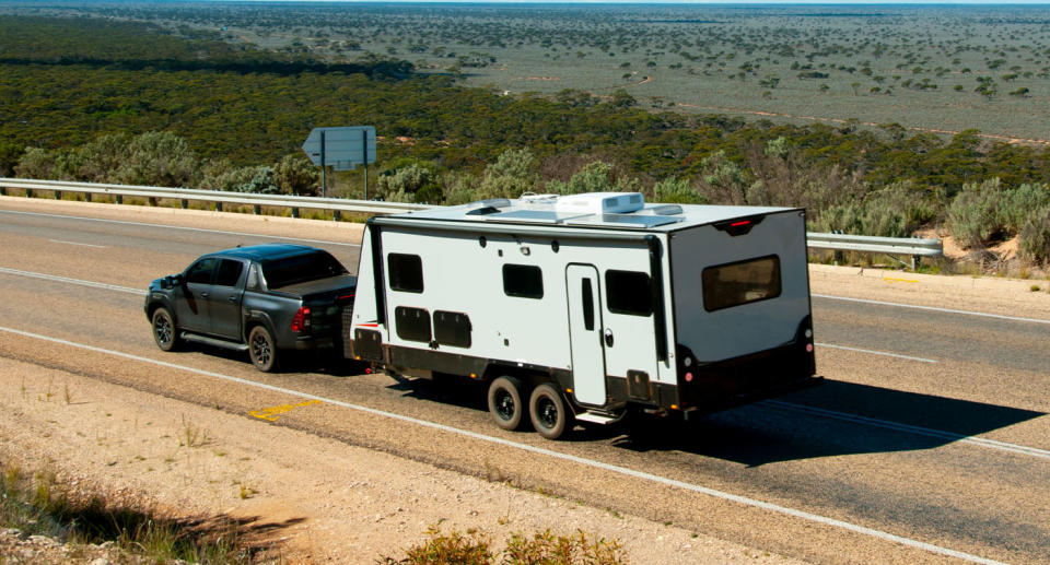 Black ute towing caravan on rural Australian road. 