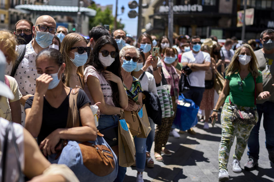 People wearing face masks stand along a street in Madrid, Spain, Thursday, June 24, 2021. Spain is easing its COVID-19 pandemic rules, permitting people to stop wearing masks outdoors and allowing sports fans back into stadiums. Almost a year after face masks became mandatory indoors and outdoors, people from Saturday will no longer be required to wear them outside as long as they can stay at least 1.5 meters (5 feet) apart. (AP Photo/Manu Fernandez)