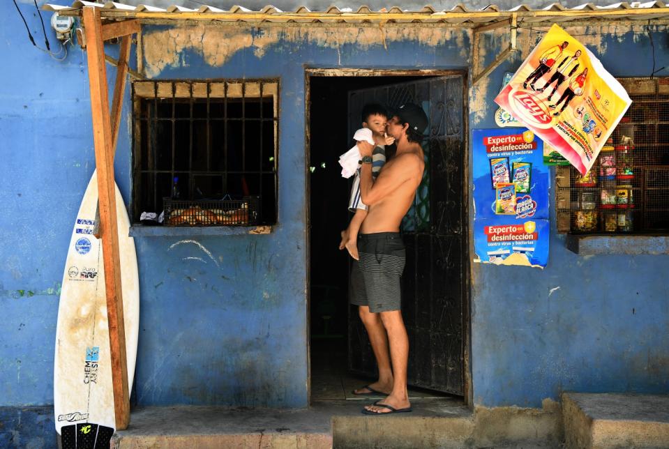 Surfer Bryan Perez holds his nephew outside his mother's store