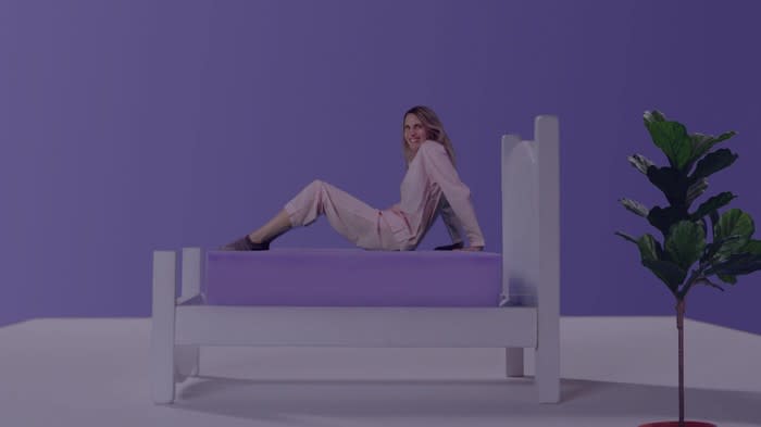Woman on a bed with a purple mattress, in a room with a purple wall.