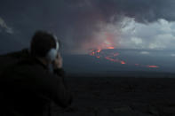 A spectator watches the lava flow down the mountain from the Mauna Loa eruption, Tuesday, Nov. 29, 2022, near Hilo, Hawaii. (AP Photo/Marco Garcia)