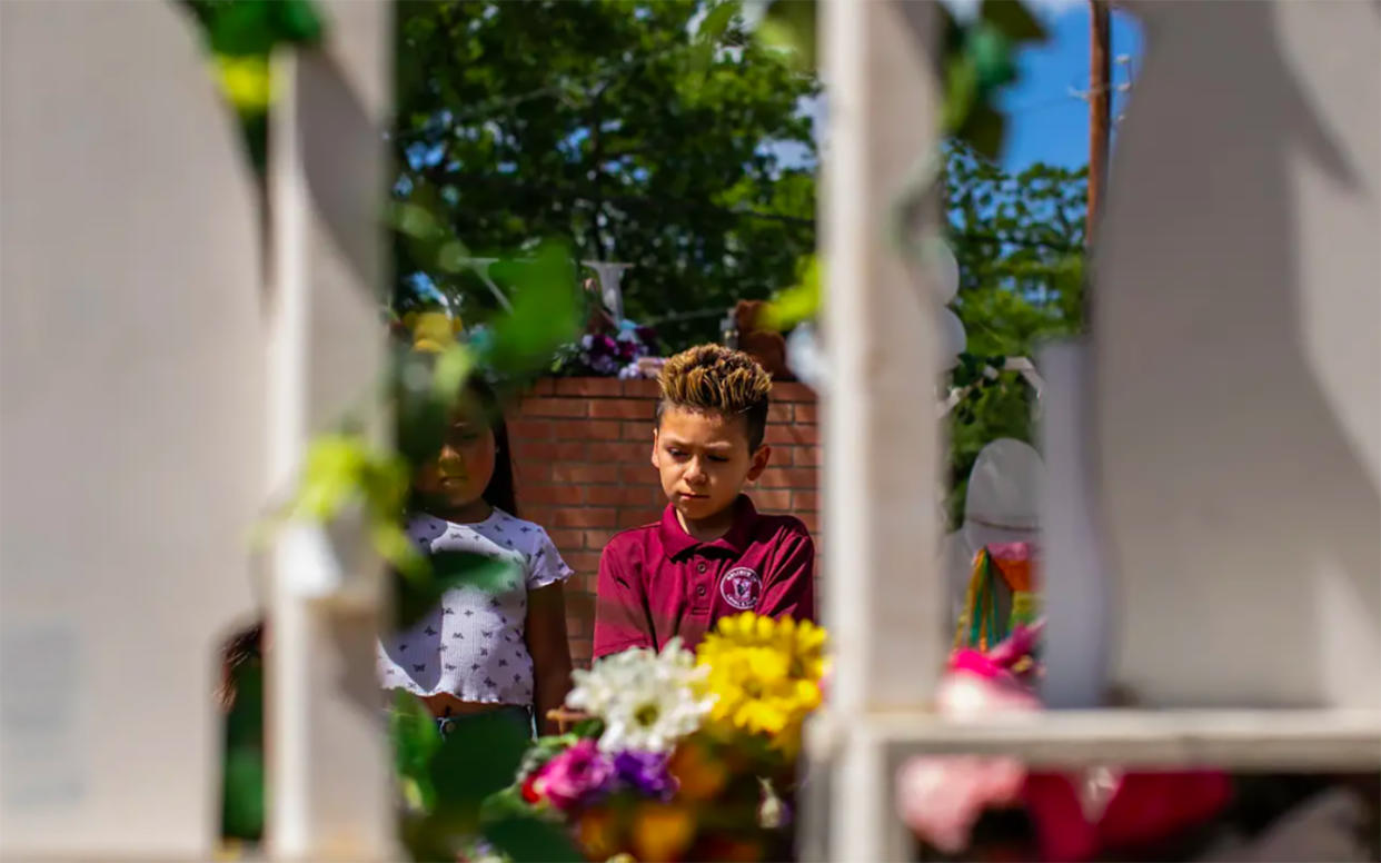 Two students gaze at piles of flowers and balloons left in front of crosses at Robb Elementary in Uvalde