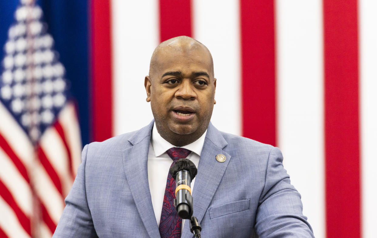 Ras Baraka, mayor of Newark, at the microphone with a background of U.S. flags,