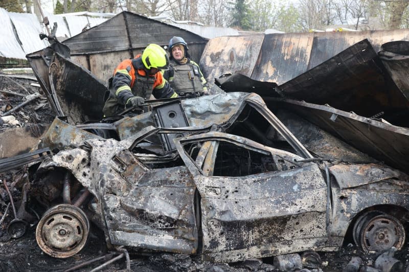 Two rescuers are seen by a burnt-out car after a Russian precision-guided munition hit civil infrastructure, Kharkiv, northeastern Ukraine. -/Ukrinform/dpa